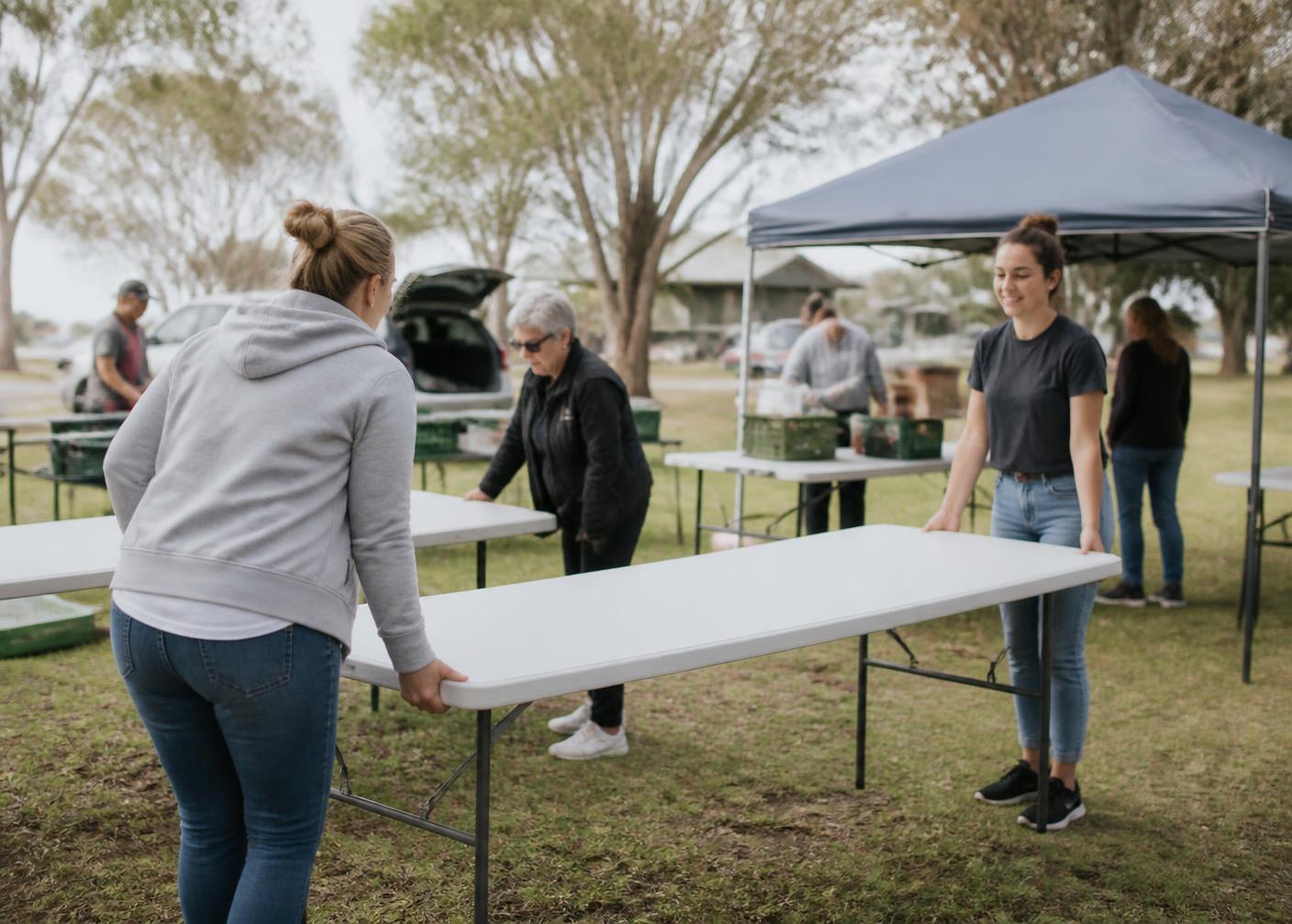 Volunteers setting up trestle tables at a community event on a grassy reserve